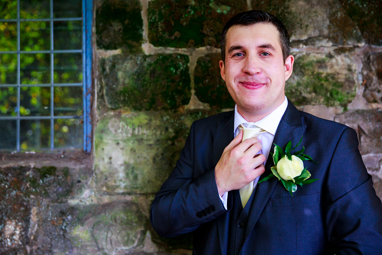 Saxon Mill Wedding Photographer - groom doing his tie against a stone wall at the Saxon Mill